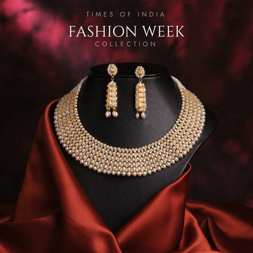 A pearl and gold necklace with matching earrings is displayed on a black stand, draped with red satin fabric. Text reads "Times of India Fashion Week Collection.