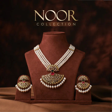 Gold and pearl necklace set with matching earrings displayed on a brown velvet stand, under a sign reading "NOOR COLLECTION" against a dark brown background.