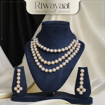 A pearl necklace set with matching earrings displayed on a navy blue stand, with the brand name "Riwayaat" at the top.