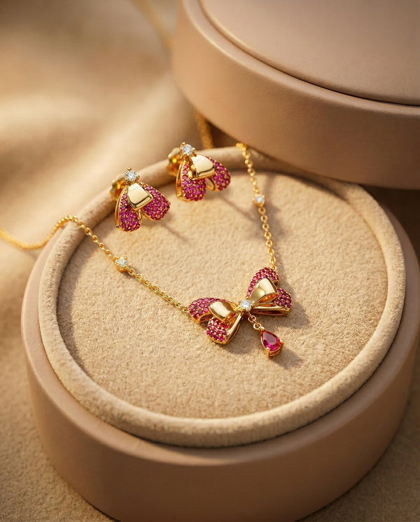 Gold necklace with pink gemstone bow pendants on a beige jewelry display box.