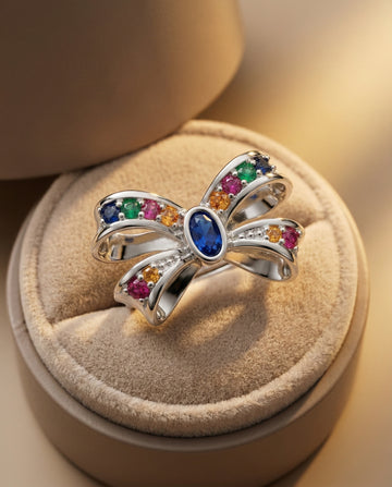Silver bow-shaped ring with colorful gemstones on a beige cushion