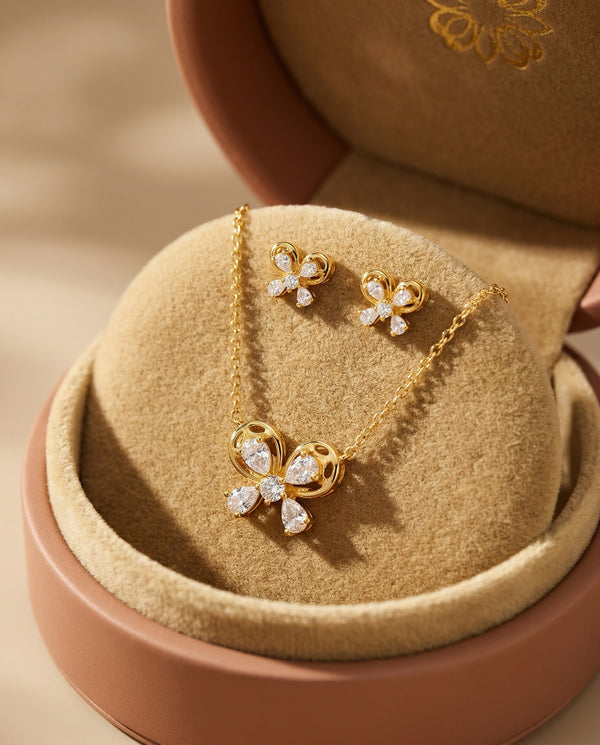 Gold necklace with floral pendant and matching earrings on a beige jewelry box.