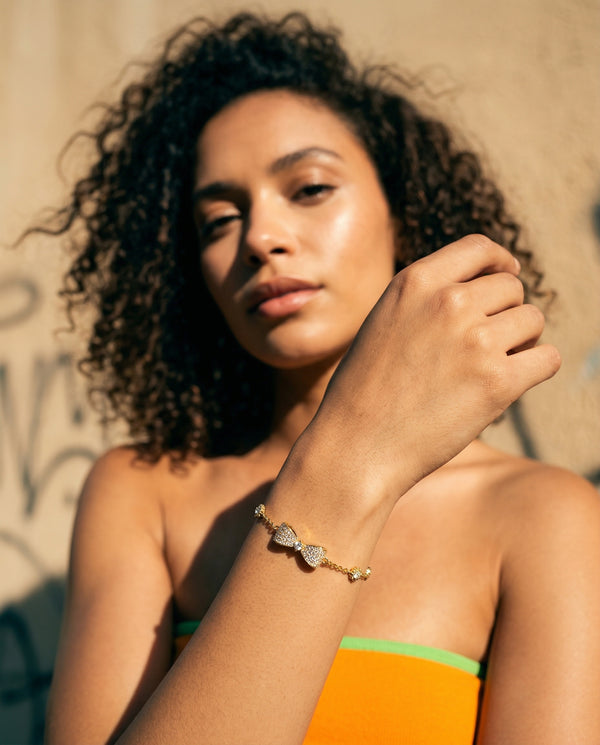 Woman wearing a gold bracelet with a textured design against a textured wall.