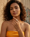 Woman wearing a gold ring with a yellow top against a textured wall.