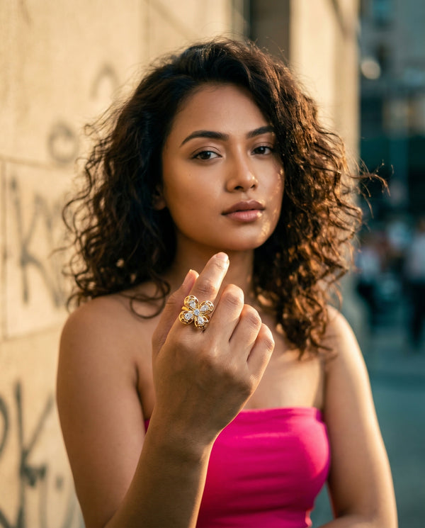 Woman in a pink top with a floral ring on her finger, standing against an urban background.