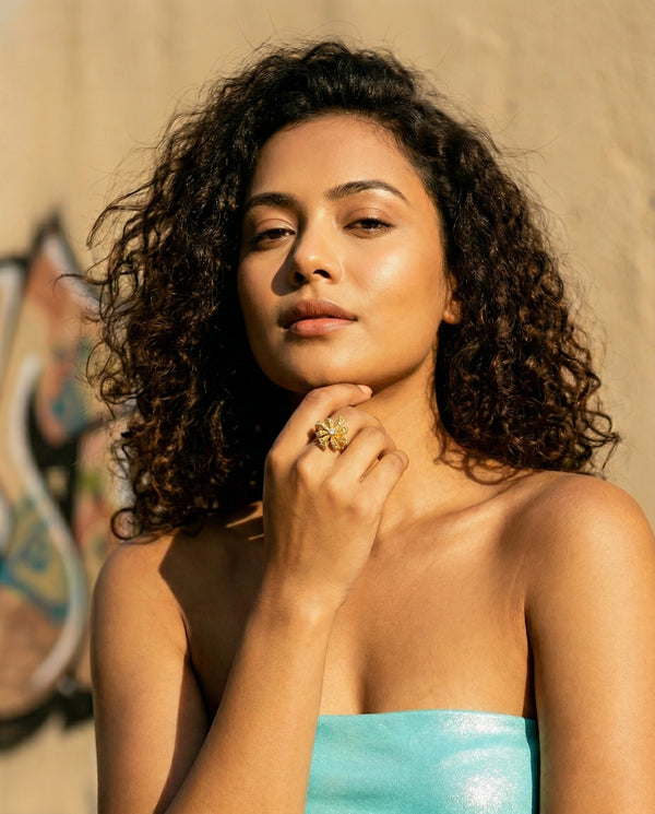 Woman with curly hair wearing a blue strapless top against a beige wall.