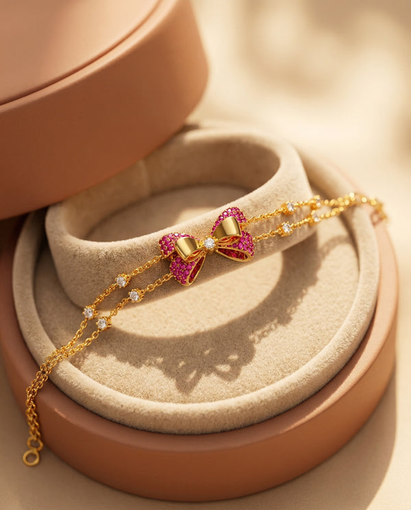 Gold bracelet with pink gemstone bow clasp on a beige jewelry display