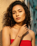 Woman in a red strapless top with a bracelet, standing against a textured wall.