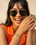 Woman wearing sunglasses and an orange outfit with a gold bracelet.