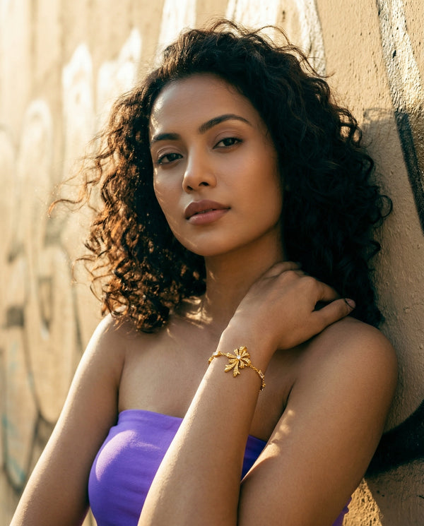 Woman with curly hair wearing a purple top against a textured wall.