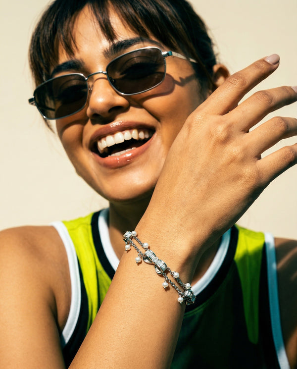Woman wearing sunglasses and a bracelet, smiling against a neutral background