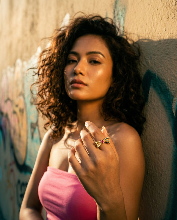 Woman with curly hair holding a pink object against a graffiti-covered wall.