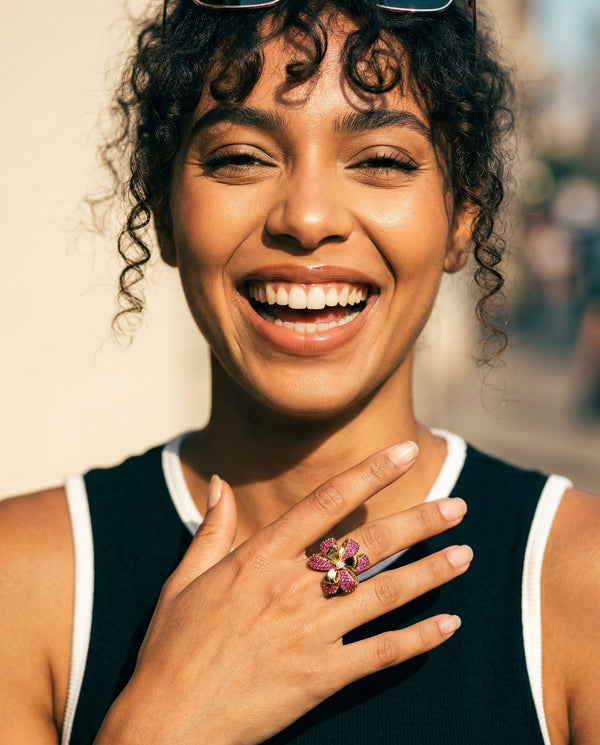 Woman wearing a pink ring with a floral design, smiling outdoors.
