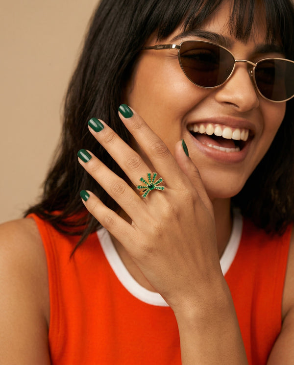 Woman wearing sunglasses and an orange top, with a green ring on her finger.