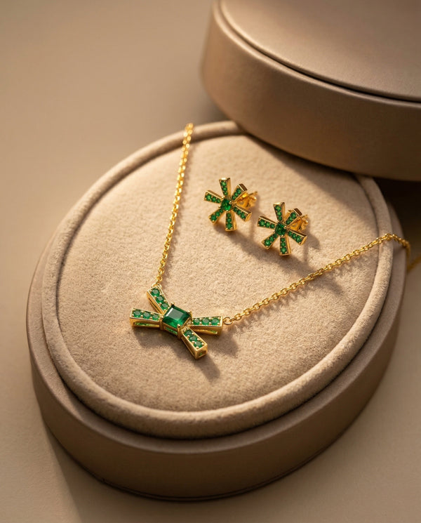 Gold necklace and earrings with green gemstones on a beige jewelry box.