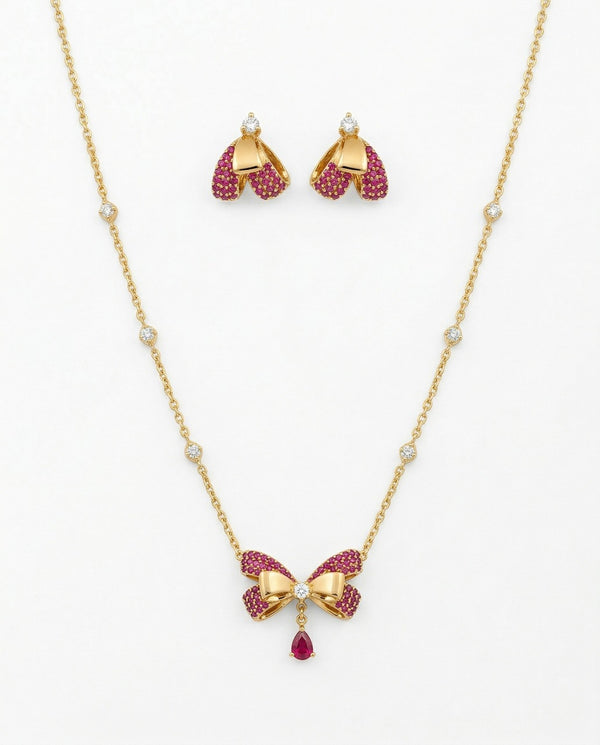 Gold necklace with bow design and pink gemstones, paired with matching earrings on a white background.