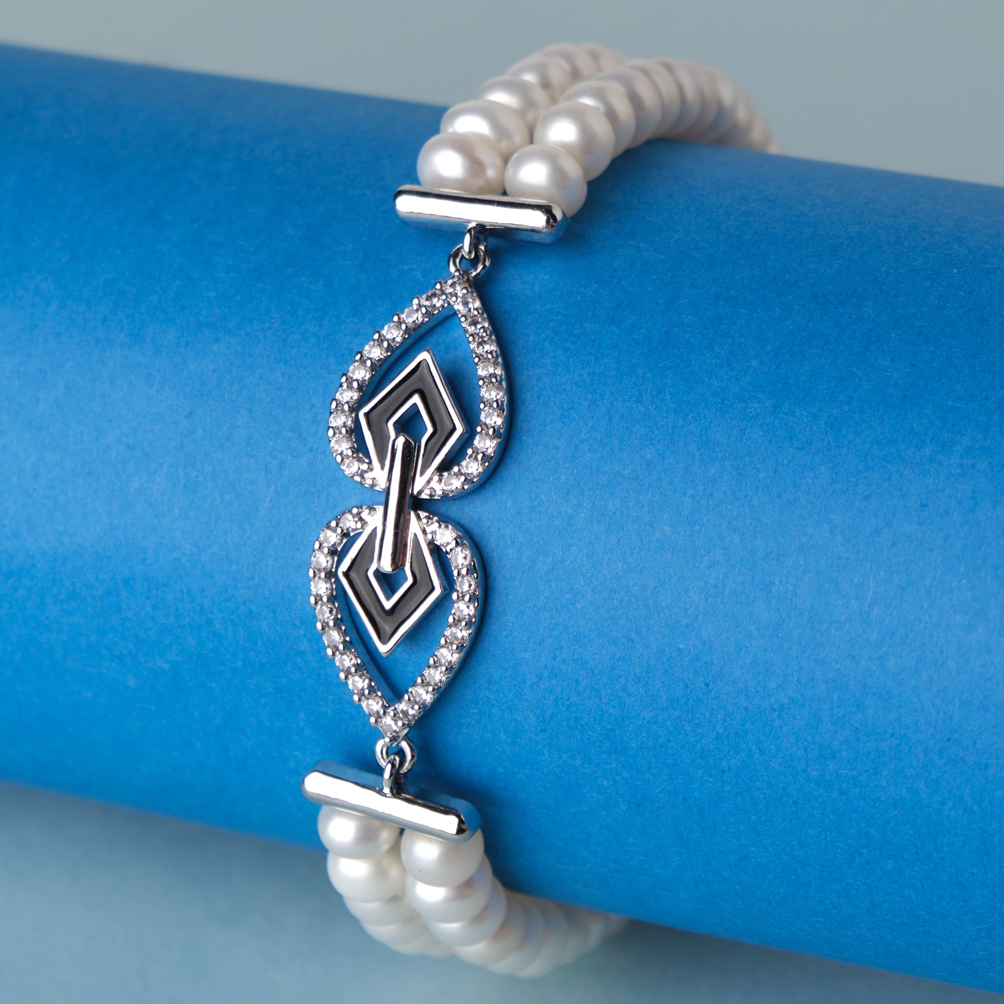 The Chandrani Pearls Modish Stone Studded Pearl Bracelet with diamonds on a blue background.
