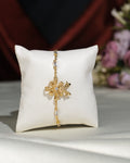 The Metallic CZ Pretty Bracelet by Chandrani Pearls India, featuring a floral design and sparkling stones, is displayed on a white cushion with blurred flowers in the background, emphasizing its unique style.