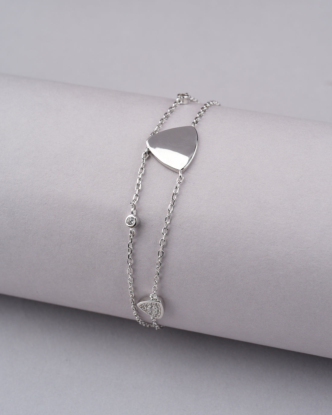 The Tvisha 925 Silver White Bracelet by Chandrani Pearls India features heart and round charms, displayed on a ribbed cylindrical surface with two red roses nearby—perfect for both casual and formal wear.