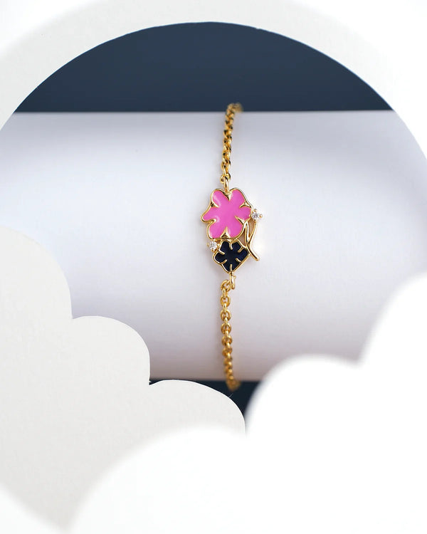 The Chandrani Pearls India Alisha Flory Chain Bracelet for kids, featuring pink and black floral charms, is displayed against a white and dark blue background.