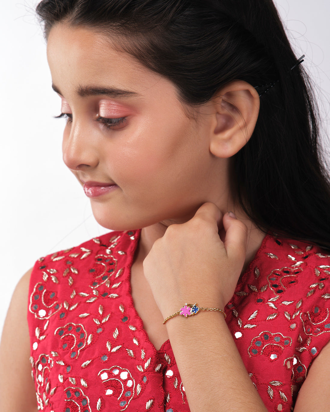 The Chandrani Pearls India Alisha Flory Chain Bracelet for kids, featuring pink and black floral charms, is displayed against a white and dark blue background.