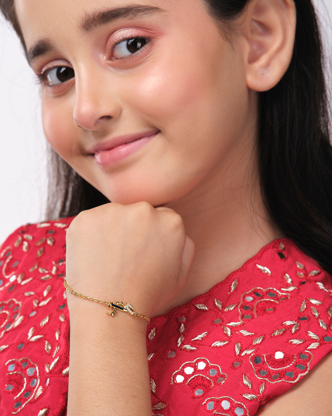 The Dainty Krishna Chain bracelet for kids by Chandrani Pearls India is displayed on a white and navy scalloped backdrop, featuring a blue gem with a leaf design.