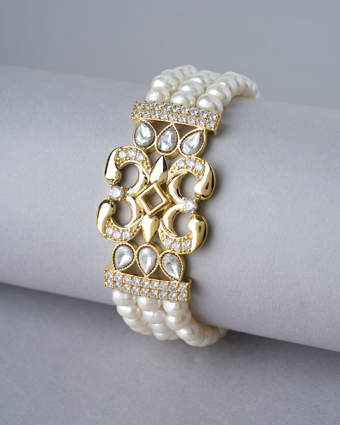 The Beautiful 3 Line Bracelet by Chandrani Pearls India, featuring pearl strands and polished silver accents, is elegantly displayed on a white cushion with blurred flowers in the background.