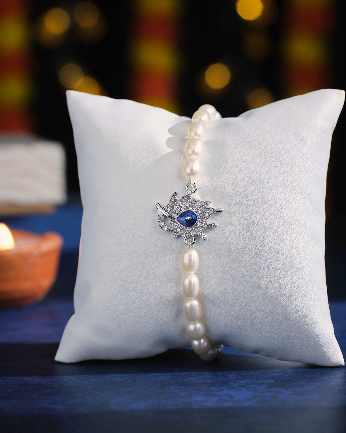 The Moonlit Delight Pearl Bracelet by Chandrani Pearls, featuring a silver hamsa charm, displayed on a white cushion.