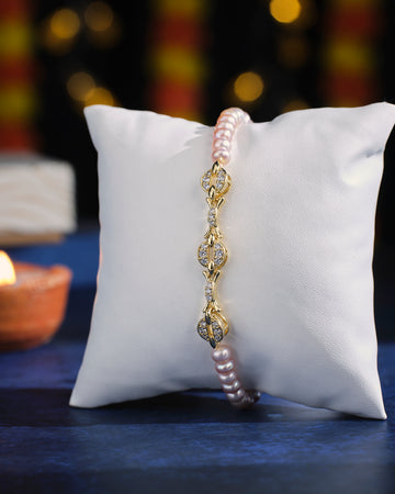 The Eternal Bond Pearl Bracelet from Chandrani Pearls features a gold and diamond-accented link chain, elegantly showcased on a white cushion against a softly blurred background with warm lighting.