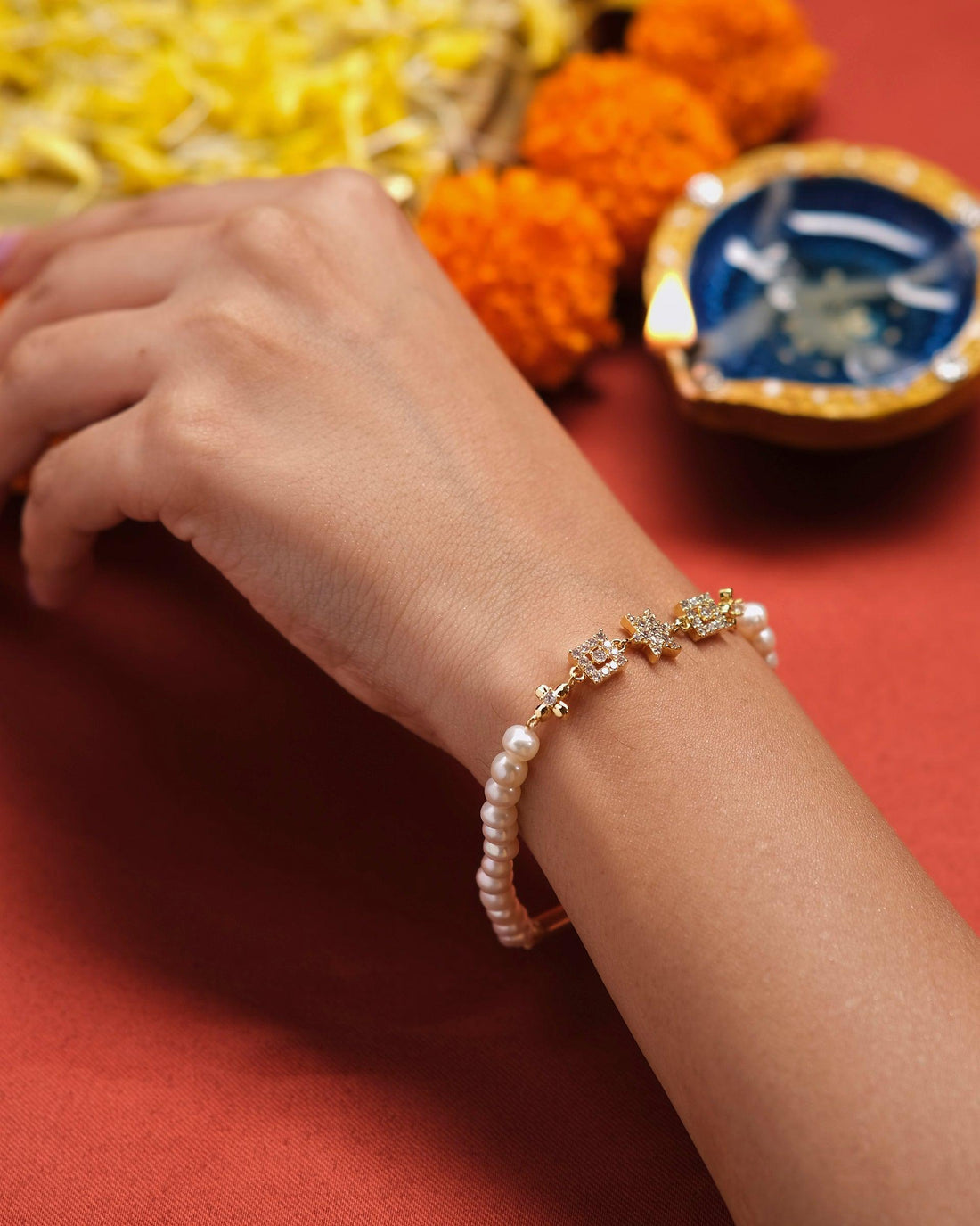 The Dagny Pear Bracelet by Chandrani Pearls, featuring star and square diamonds, is elegantly displayed on a white cushion beside an unlit candle on a blue surface.