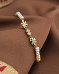 The Noor Soft Glow Bracelet by Chandrani Pearls, featuring delicate pearls and floral CZ accents, is displayed on a brown fabric background.