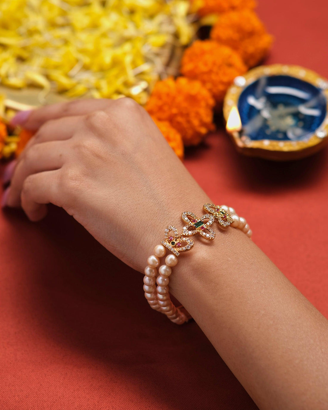The Bewitching Butterflies Pearl Bracelet by Chandrani Pearls is elegantly showcased on a white cushion, set against a backdrop of softly blurred lights.