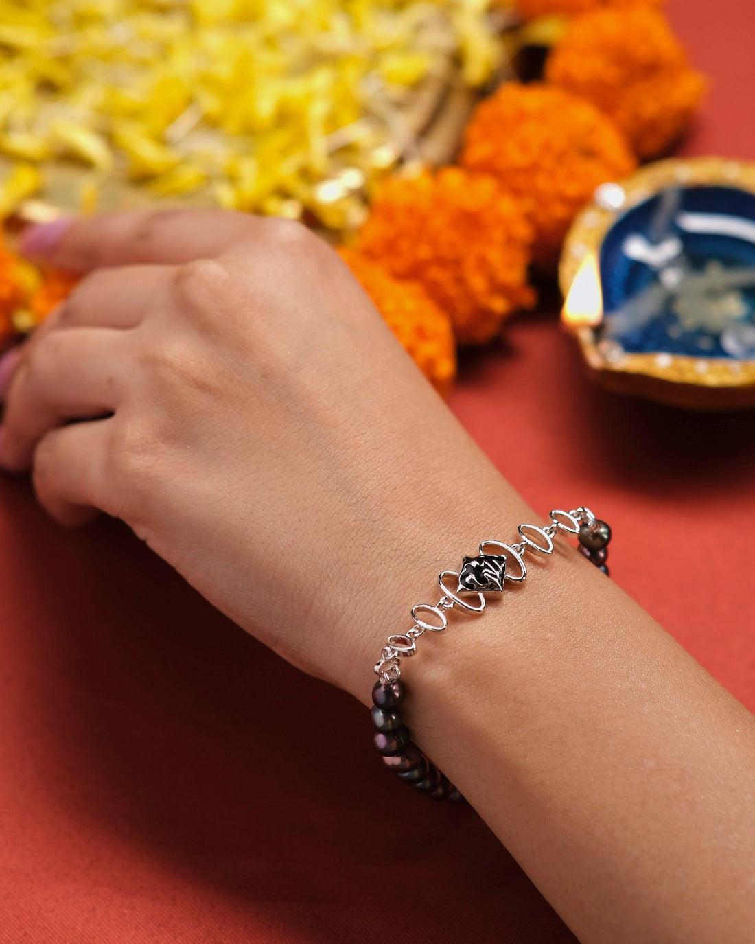 The Curb Link Station Pearl Bracelet by Chandrani Pearls, featuring a silver band and a black centerpiece, is elegantly showcased on a white cushion against a softly blurred dark backdrop.
