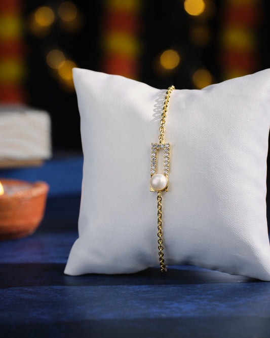 The Chain Reaction Pearl Bracelet by Chandrani Pearls, featuring a rectangular pendant adorned with small crystals and a pearl, displayed on a white cushion against a dark blue background.