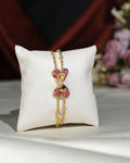 The Cute Metallic CZ Pretty Bracelet by Chandrani Pearls India features a bow-shaped centerpiece with pink and white stones, ideal for formal or casual wear, and is elegantly displayed on a white cushion.