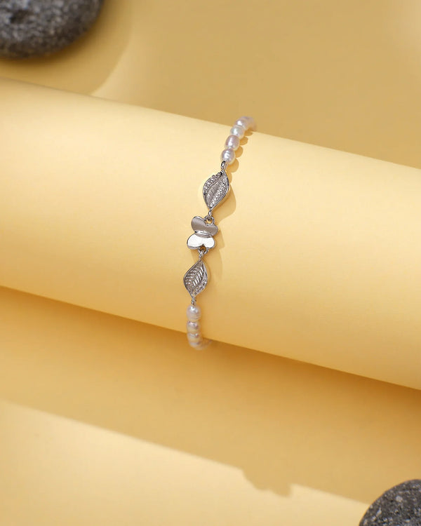 The Elegant Pearl & CZ Tennis Bracelet Rodium Finish by Chandrani Pearls is shown on a yellow background with decorative stones, featuring a refined design for an elegant look.