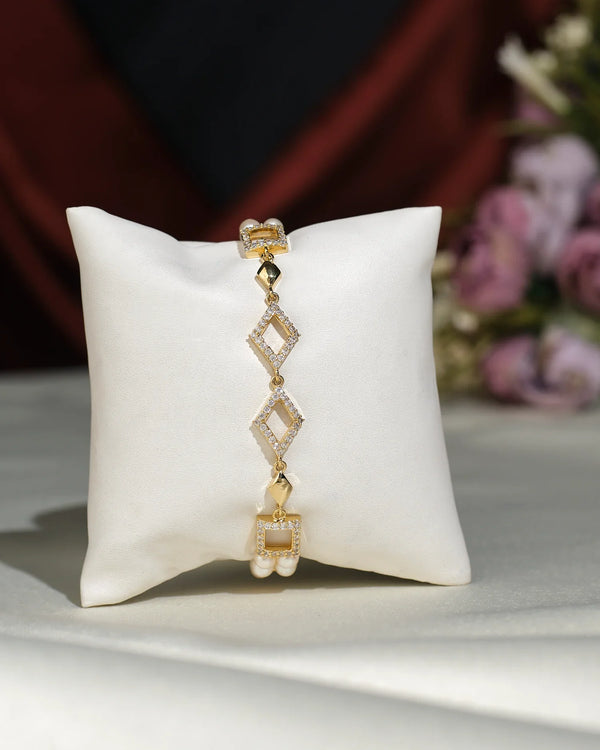 The Regal Pearl Bracelet by Chandrani Pearls India showcases elegant gold and diamond geometric design with pearl accents, displayed on a white cushion with soft, blurred flowers in the background.