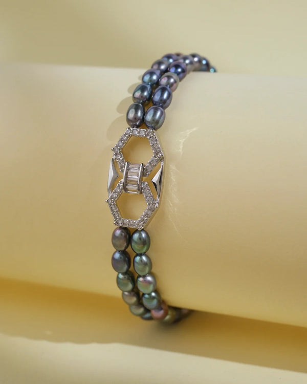 The Trendy Black 2 Line Pearl Bracelet by Chandrani Pearls India features elegant double strands of black pearls and a geometric silver clasp with diamonds, perfectly showcased on a light yellow surface for everyday luxury.