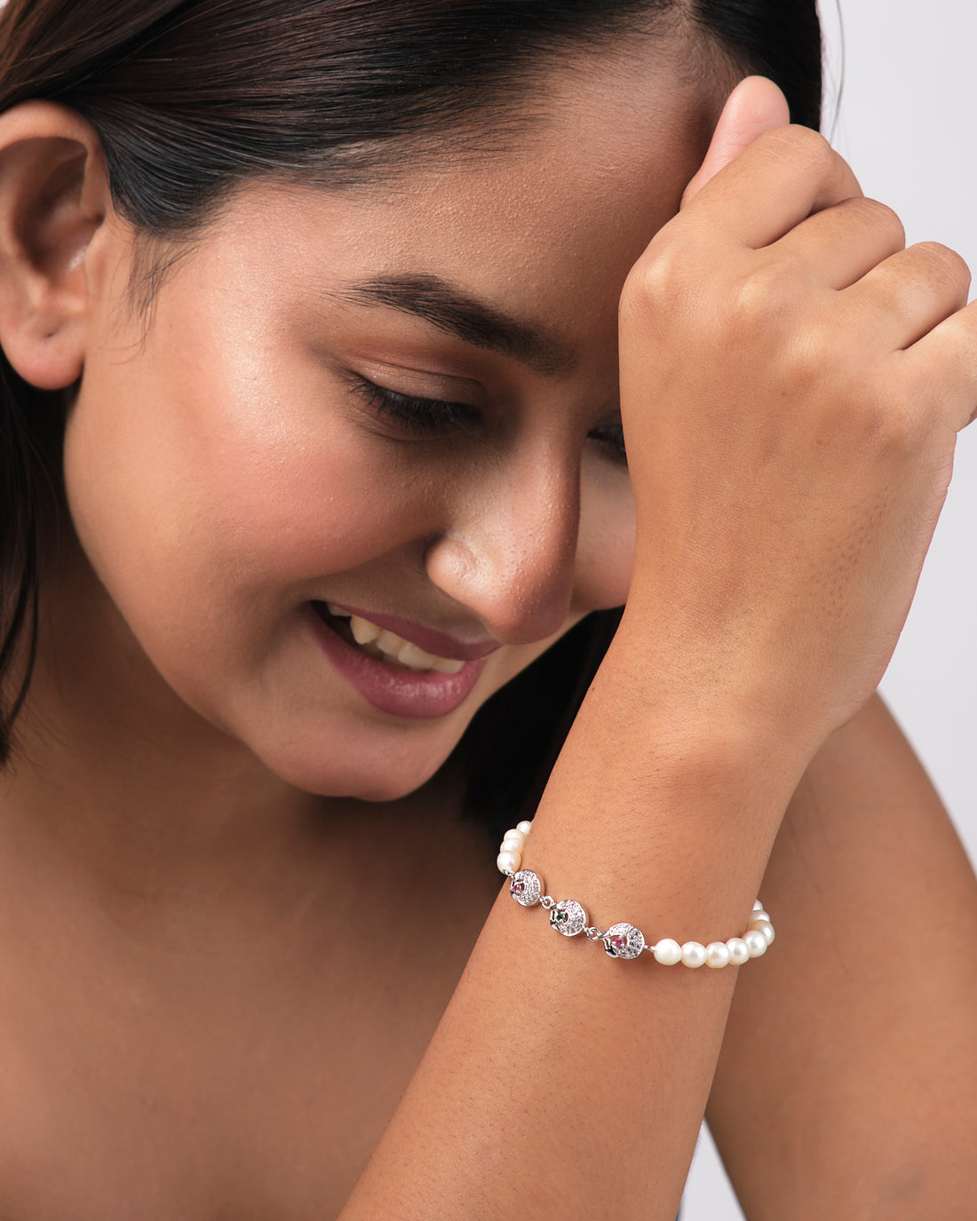 The Pretty White 1 Line Pearl Bracelet by Chandrani Pearls India features elegant pearls and three silver pendants with colored stones, shown on a light yellow background—an ideal choice for everyday luxury.