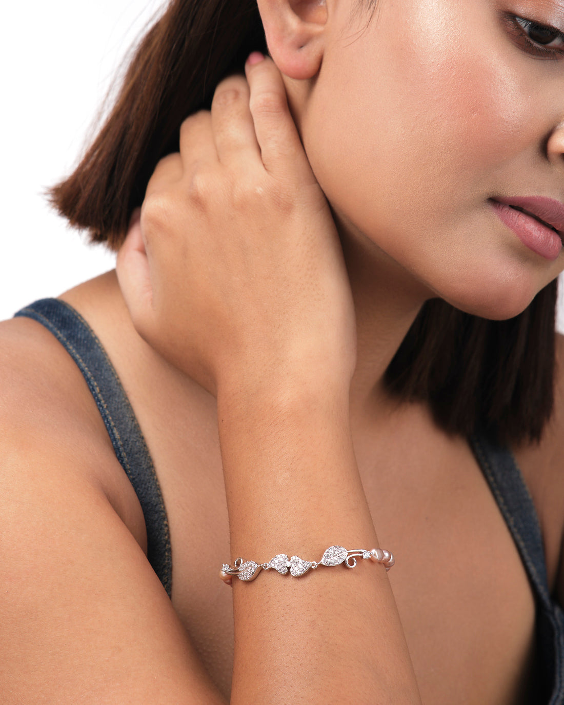 The Leafy Pink1 Line Pearl Bracelet by Chandrani Pearls India, featuring leaf-shaped links and pearls, displayed on a light yellow cylindrical surface, embodies the elegance and simplicity of refined jewelry design.