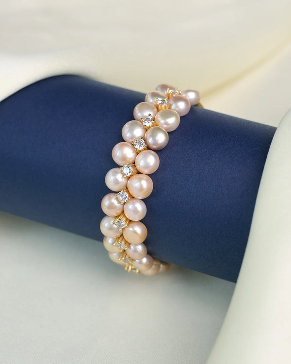 The Lustrous Pearl & Cubic Zirconia Bracelet by Chandrani Pearls is showcased on a dark blue cylinder against a cream fabric backdrop, featuring alternating luminous pearls and sparkling cubic zirconia accents.