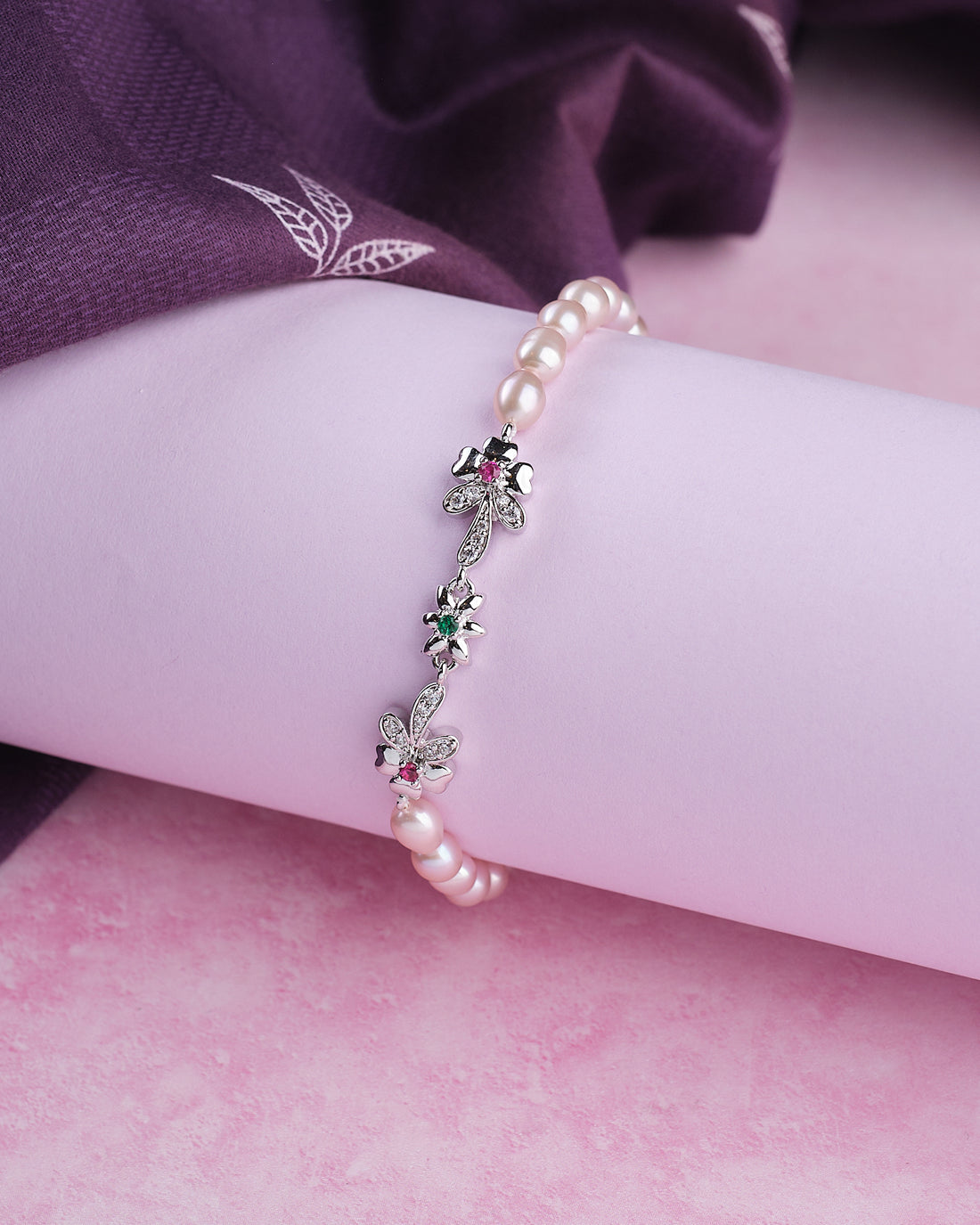Chandrani Pearls’ Trendy Metallic CZ Pretty Bracelet: A chic bracelet with metallic and CZ details, displayed on a rolled white surface and complemented by soft purple fabric in the background.