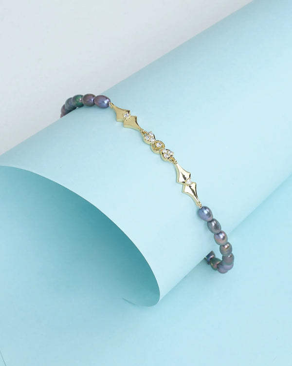 Classic elegance in every pearl by Chandrani Pearls: a gold and pearl bracelet with geometric diamond accents and sparkling CZ stones, showcased on a curved light blue background.