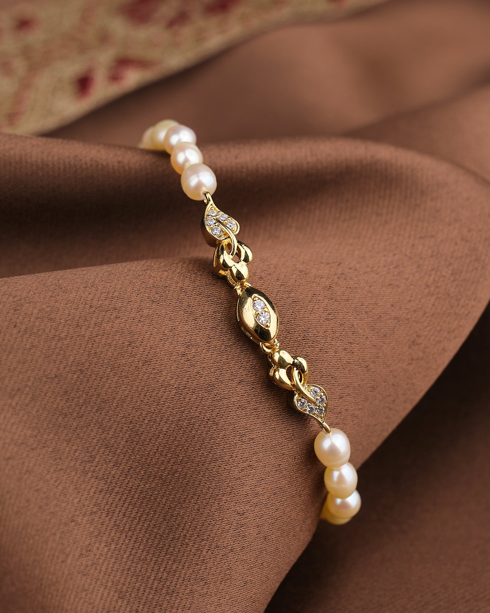 The Noor Pink Light Pearl Bracelet by Chandrani Pearls features blush-toned pearls and CZ stones, displayed on brown fabric—an elegant choice for lovers of feminine jewelry.