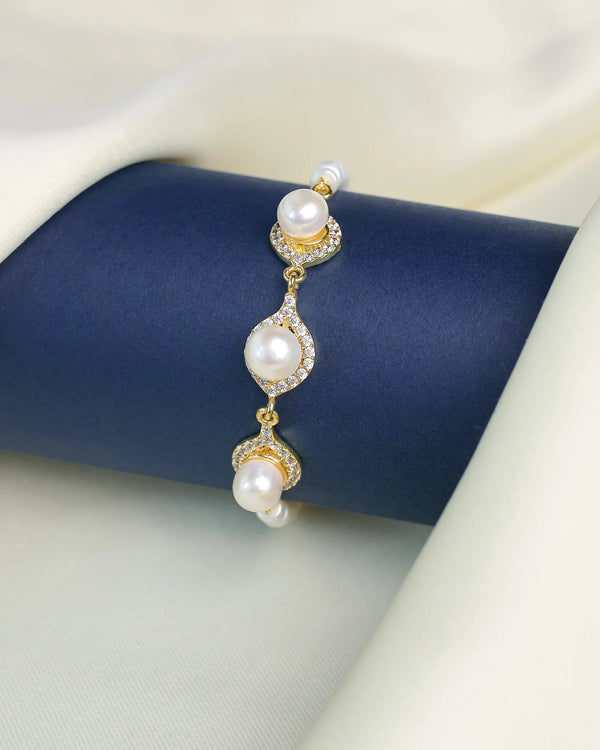 The Classic Beauty Pearl Bracelet with CZ Detailing from Chandrani Pearls is displayed on a dark blue cylindrical stand, surrounded by cream-colored fabric. Elegant pearls and sparkling cubic zirconia create a timeless look.