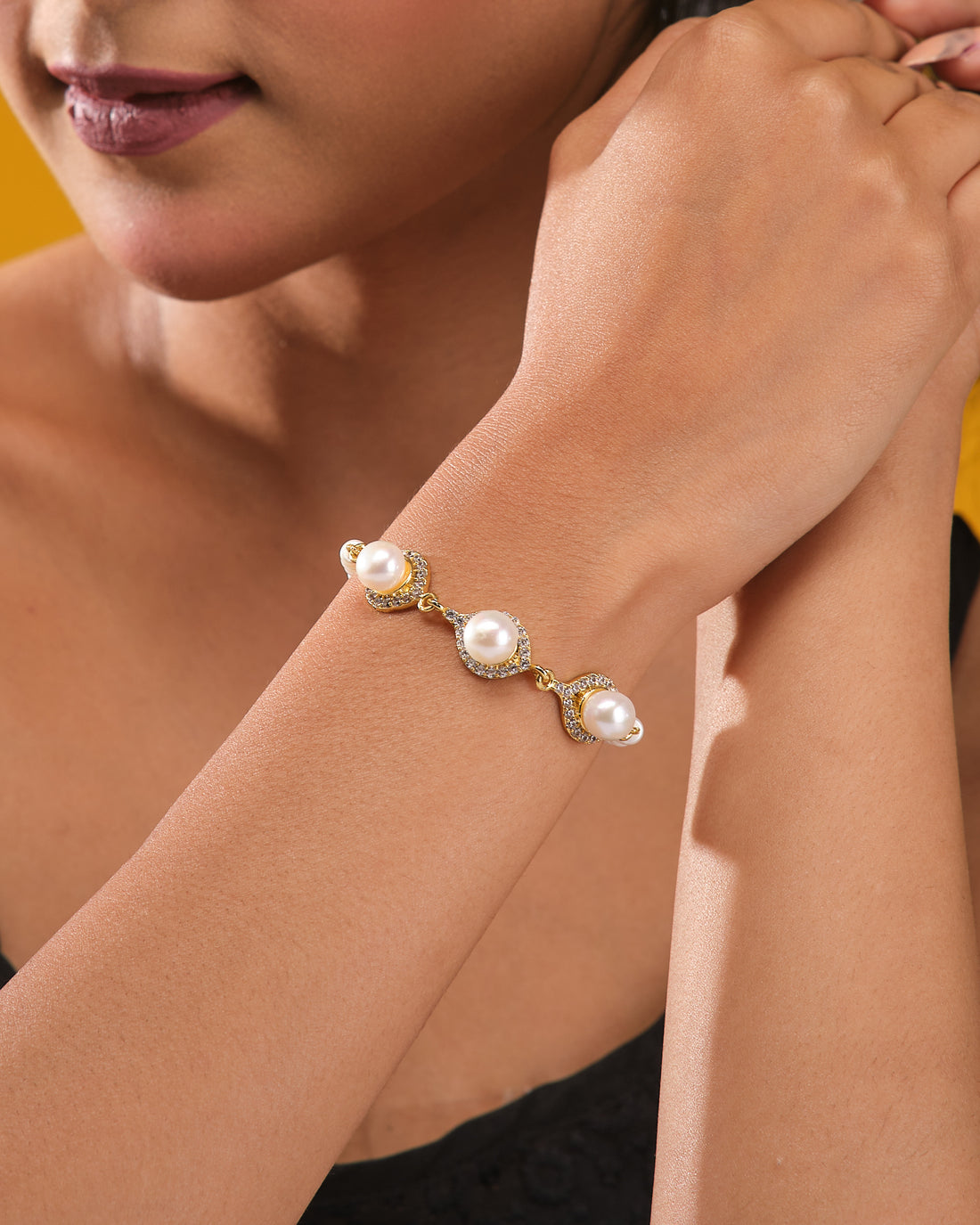 The Classic Beauty Pearl Bracelet with CZ Detailing from Chandrani Pearls is displayed on a dark blue cylindrical stand, surrounded by cream-colored fabric. Elegant pearls and sparkling cubic zirconia create a timeless look.
