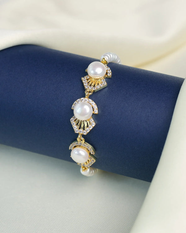 The Chandrani Pearls Luxury Pearl Bracelet with CZ Accents features three fine pearls and sparkling CZs, elegantly displayed on a dark blue cylindrical stand draped in cream fabric.