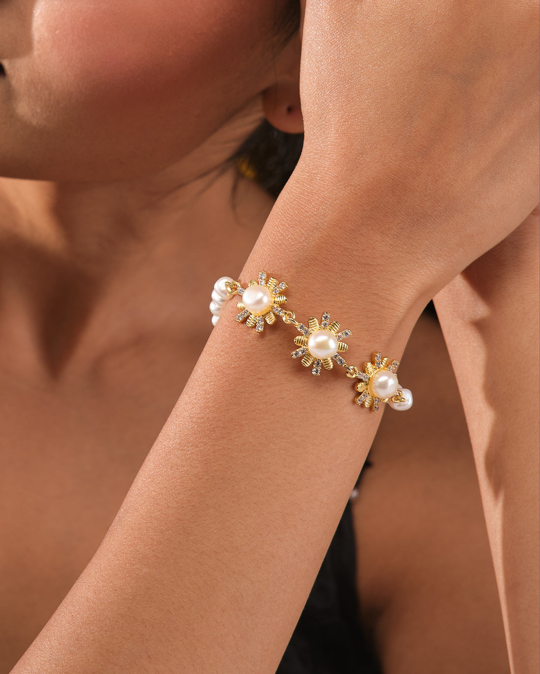 The Graceful Pearl & CZ Link Bracelet by Chandrani Pearls features daisy-shaped flower links with pearl centers and cubic zirconia, displayed on a navy blue holder against a cream fabric background.