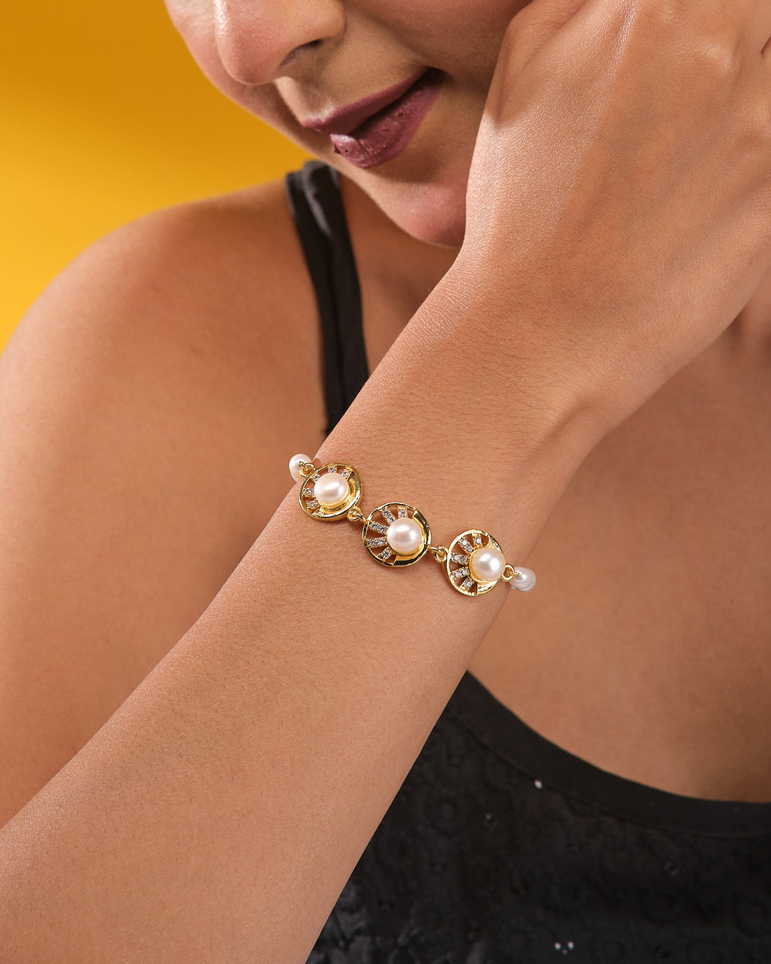 The Chandrani Pearls Radiant Pearl Bracelet with High-Polish CZ features three round pearls and sparkling cubic zirconia, shown on a dark blue cylindrical stand against cream fabric to showcase its refined finish.