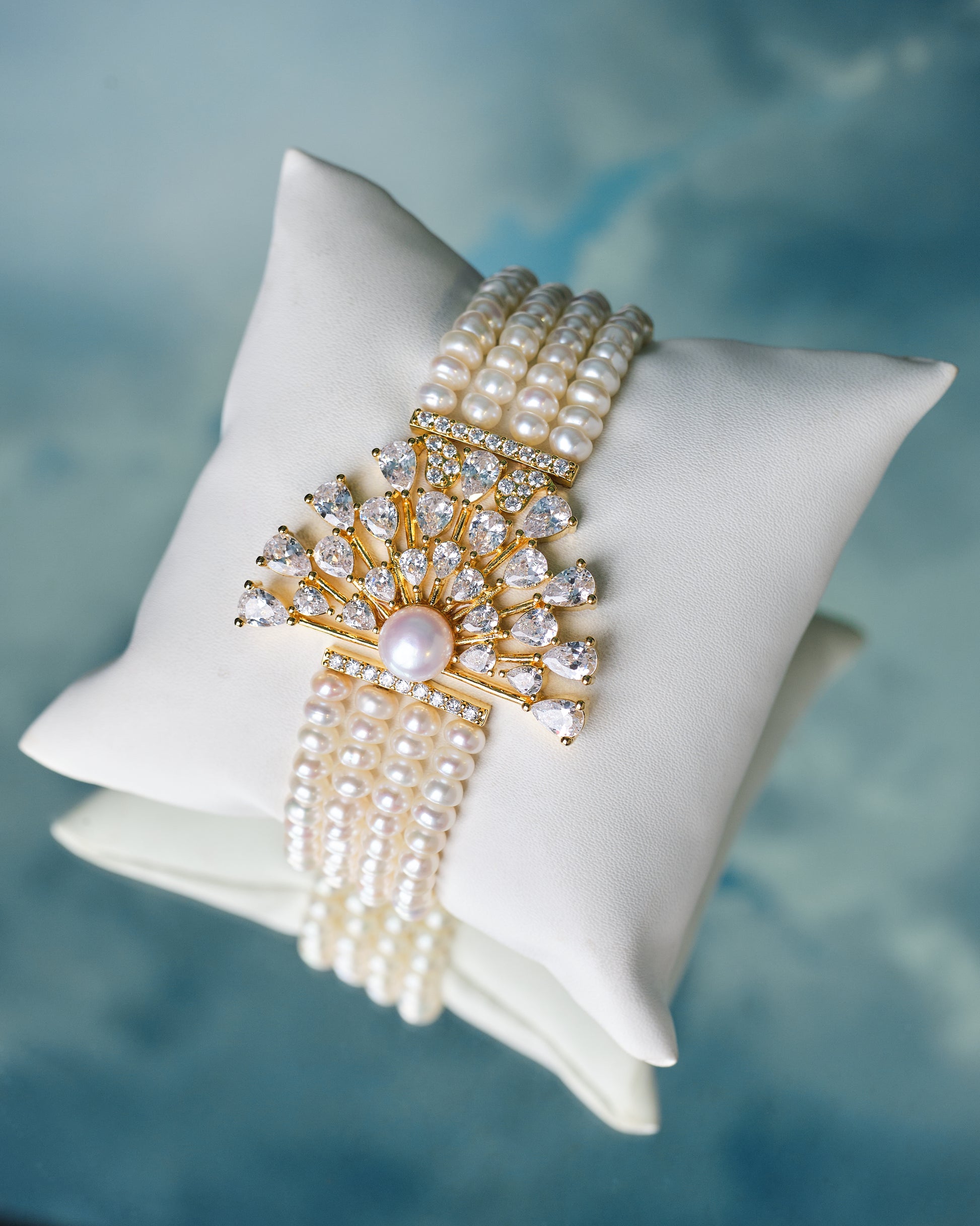 The Gorgeous Real Pearl & CZ Bracelet by Chandrani Pearls features real pearls and sparkling cubic zirconia in a fan-shaped design, displayed on a white cushion—an elegant choice for wedding jewelry.